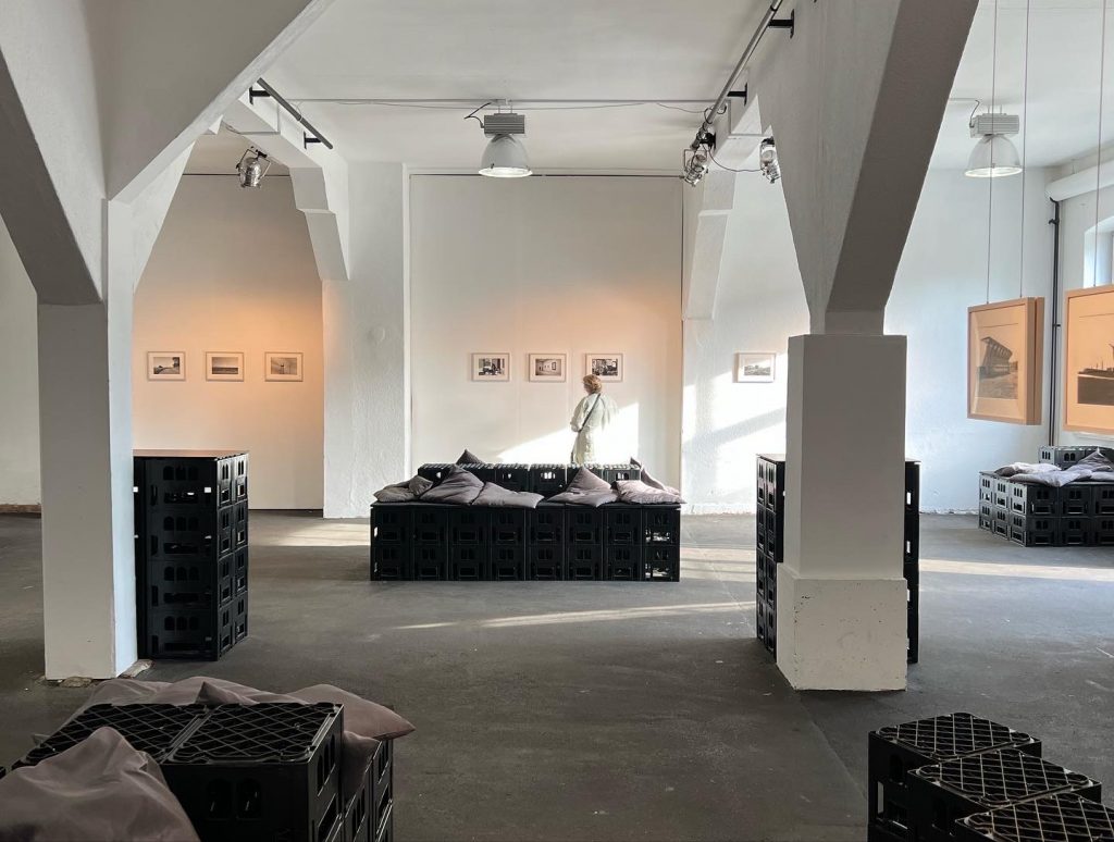 image für website von cratedesign_dem event mobiliar zum mieten aus ungelabelten getraenkekisten_mit der beschriftung_img-cratedesign-website-mobiliar-setup-ausstellung ronny waleska-innen mit Besucherin