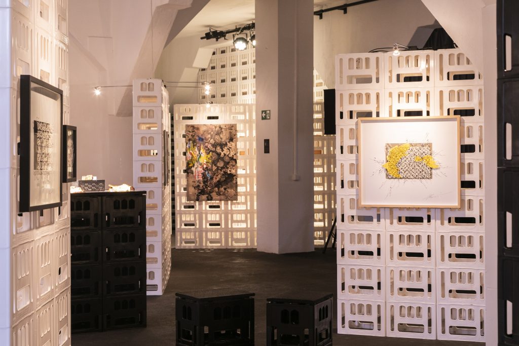 Ausstellungsdesign aus cratedesign® zur Kunstausstellung von Alabaster Becher im KOMPLEX45, mit beleuchteten Wänden an denen Gemälde befestigt sind.