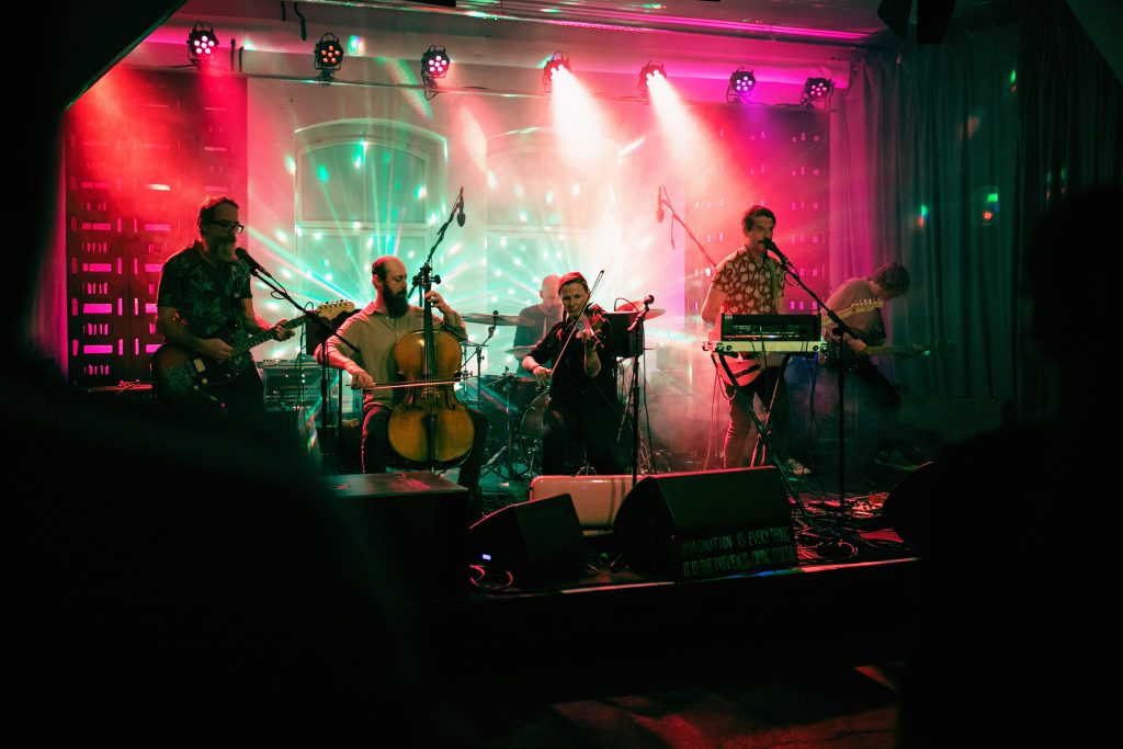 Band Nauzea Orchestra auf der Bühne im KOMPLEX45, die aus cratedesign® Kisten gebaut wurde, mit bunten Lichtern, während der Tschechisch-Deutschen Kulturtage.